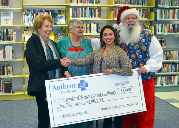 Wilma Humason, with Friends of the Kings County Library, accepts a $5,000 check from Anthem Blue Cross representative Selina Escobar for the library's summer reading program as Santa and Mrs. Claus watch.
